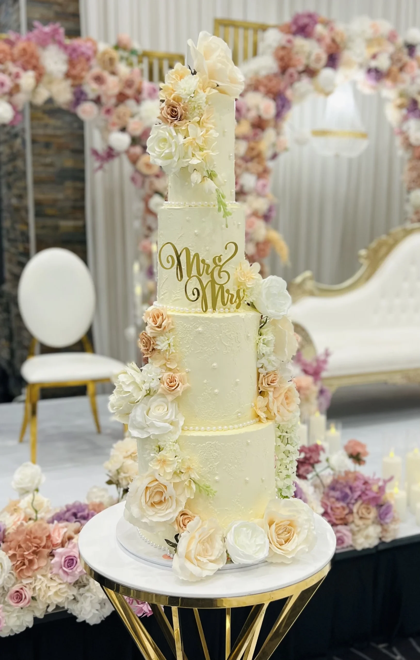 four tier wedding cake with flowers all over on a stand.