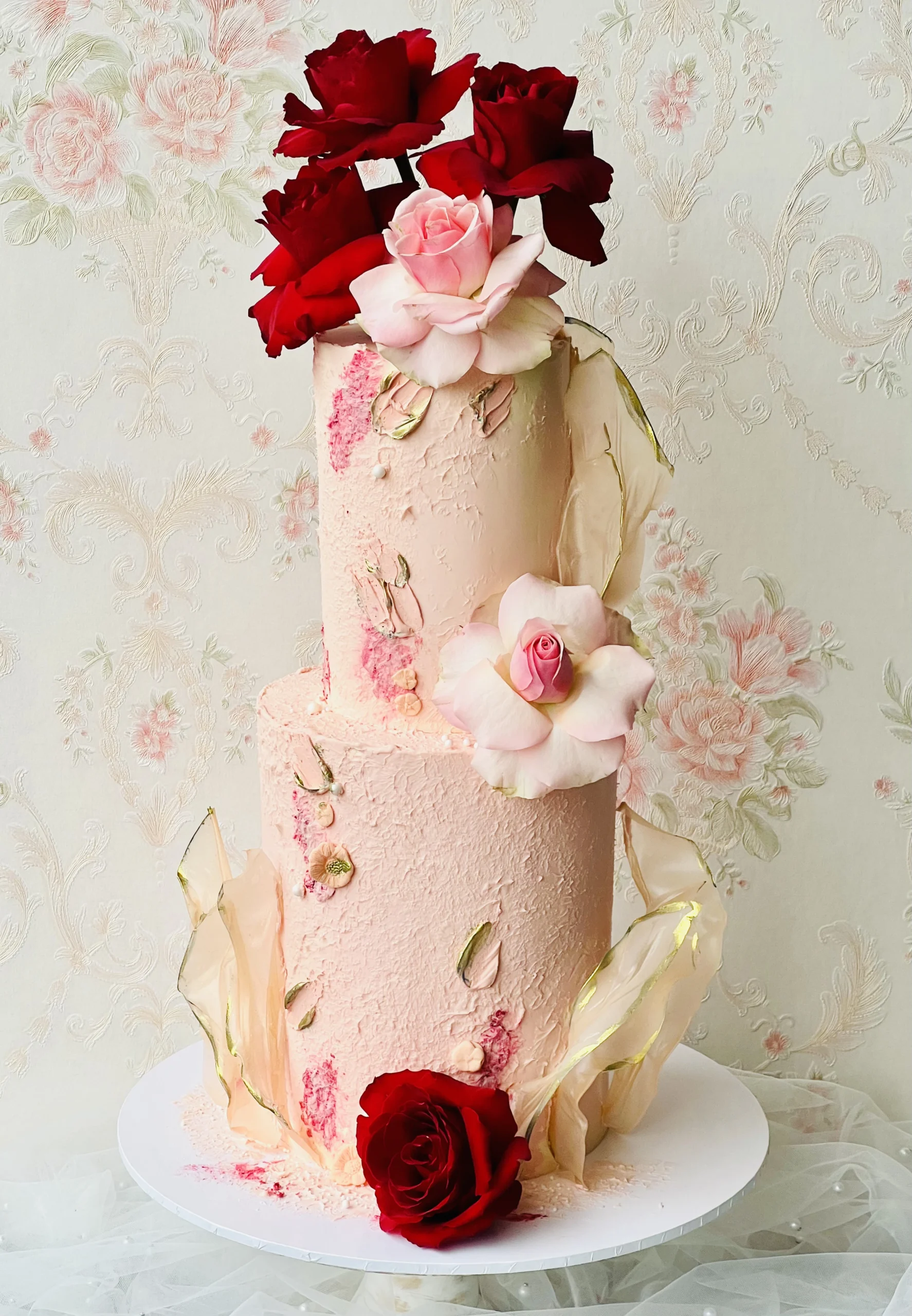 Pink two tier wedding cake with red flowers.